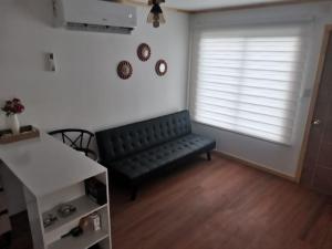 Una sala de estar con un sofá negro y una ventana. en Cabaña Osorno en pleno campo, en Osorno
