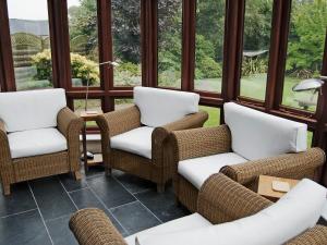 a screened in porch with wicker chairs and windows at Prideaux Farmhouse in Luxulyan