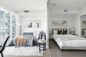 a white bedroom with two beds and a chair at Stylish 1BR Condo in the heart of the Downtown TO in Toronto