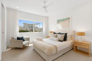 a white bedroom with a bed and a chair at Beachfront Penthouse with Private Rooftop, BBQ, 2Car in Gold Coast