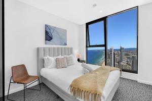 a white bedroom with a bed and a chair and a window at Newest Views On The Beach in Gold Coast