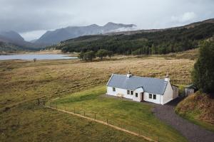 une maison blanche dans un champ à côté d'un lac dans l'établissement Torran Cottage, à Achnashellach Station
