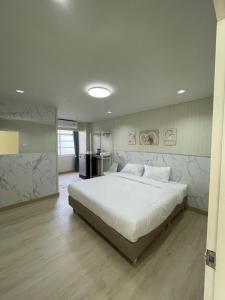 a bedroom with a large white bed and a kitchen at ปากช่องอพาร์ทเม้นท์ in Pak Chong