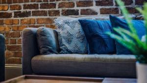 a couch with blue pillows in front of a brick wall at Central Warehouse Apt - Sleeps 8, Pet Friendly in Liverpool +17 photos