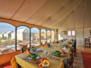 a dining room with tables and chairs and windows at Luxury Dune's Camp in Merzouga