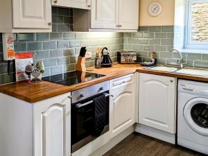 a kitchen with white cabinets and a washer and dryer at May Cottage in Hackness
