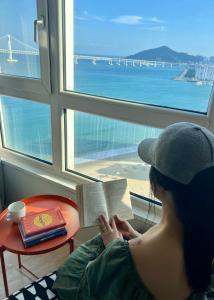 una mujer leyendo un libro delante de una ventana en Entire Studio Apartment - Busan Gwangalli Beachfront Bliss 광안리 드림홈, en Busan 18 fotos más