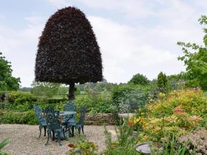 a table and chairs in a garden with a large tree at Bakery Cottage in Ampney Crucis +3 photos