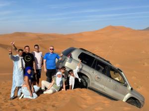 a group of people standing in the desert next to a car at Porte De Sahara Ouzina in Ouzina