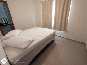 a bedroom with a bed with white sheets and a window at Summer Suites Casa Arraial do Cabo in Arraial do Cabo