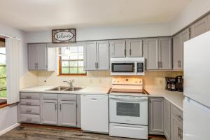 a kitchen with white cabinets and a sink and a microwave at Hillside Home 5 Mi to the Ark in Williamstown! in Corinth