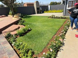 eine Frau, die durch einen Garten mit Gras und Blumen geht in der Unterkunft Queen Nanikie Guest House in Mooinooi + 2 Fotos