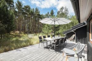 eine Holzterrasse mit einem Tisch, Stühlen und einem Sonnenschirm in der Unterkunft 2706 Nexø - Harevej 11 in Neksø