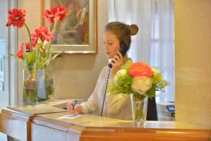 a woman talking on a phone at a desk with flowers at Hôtel Renoir Montparnasse in Paris