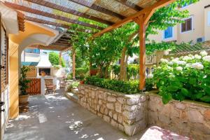 eine Terrasse mit einer Steinmauer und einer hölzernen Pergola in der Unterkunft Apartments Enna in Mali Lošinj
