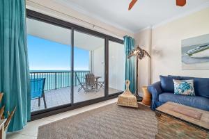 a living room with a blue couch and a balcony at Grand Pointe Unit 706 in Orange Beach