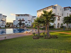 ein Gebäude mit Palmen vor einem Pool in der Unterkunft Très Joli Appartement en résidence avec piscine in Cabo Negro