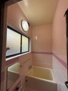 a bathroom with a tub and a window and pink tiles at 京町レジダンス in Echizen