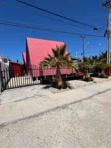 a red building with palm trees in front of a fence at Tropical Cabaña B in Coquimbo +2 photos