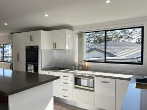 a kitchen with white cabinets and a large window at The Branch by the Basin Family Escape with Sunset Views in St Georges Basin