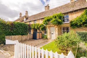 una vieja casa de ladrillo con una valla blanca en Historic 3 Bedroom Cottage in the Cotswolds, en Idbury