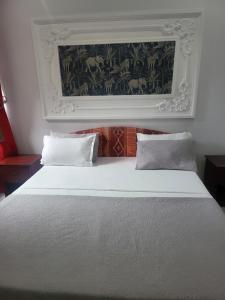 ein Schlafzimmer mit einem weißen Bett und einem Gemälde an der Wand in der Unterkunft Étoile de Justin in Pointe-Noire