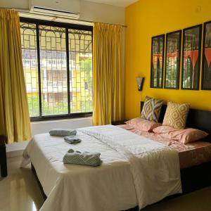 a bedroom with a large bed with yellow walls and windows at Cozy Corner - Tropical 2BHK pool pad in Varca +21 photos