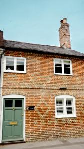a brick building with a green door and two windows at Hazelbury Cottage in Wilton