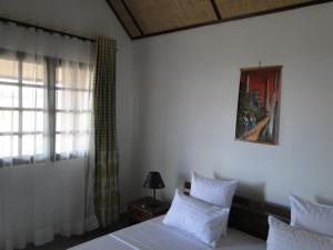 Schlafzimmer mit einem Bett mit weißer Bettwäsche und einem Fenster in der Unterkunft HOTEL H1 ISALO in Ranohira