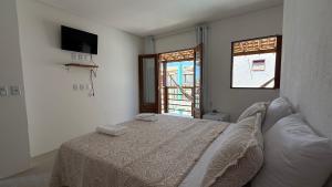 a white bedroom with a bed and a window at Chalé Sol Nascente Milagres in São Miguel dos Milagres