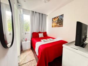 a small bedroom with a red bed and a tv at Hospedagem no Farol da Barra in Salvador