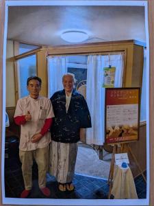 two older men standing in a room with a sign at Guest house AIZU First in Aizuwakamatsu