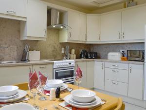 una cucina con armadi bianchi e un tavolo con piatti e bicchieri di Mill Shore Cottage - 26817 a Pennan