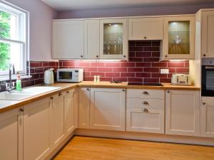 a kitchen with white cabinets and a brick wall at Roseburn Cottage in Moffat