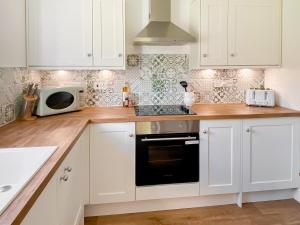 eine Küche mit weißen Schränken und einer Mikrowelle in der Unterkunft Rose Cottage in Blakemere