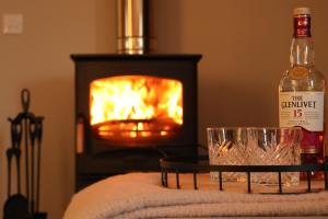 a bottle of whiskey and a glass next to a fireplace at Remore Steading - The Coach House in Ardclach