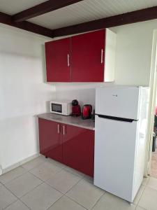 a kitchen with red cabinets and a white refrigerator at Charmant F2 créole in Sainte-Luce +5 photos