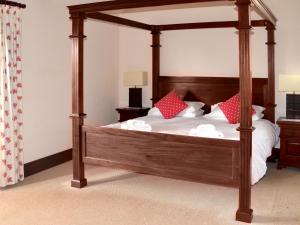a bedroom with a wooden canopy bed with red pillows at Kingfisher Barn in Sculthorpe +20 photos