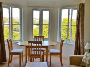 a living room with a table and chairs and windows at Meadowside Apartment in Fowey