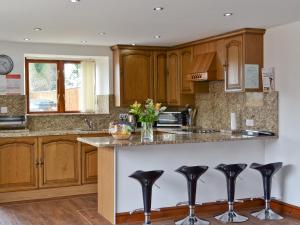 a kitchen with wooden cabinets and black bar stools at Roslyn Cottage in Hamsterley