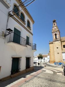 a white building with green doors and a clock tower at Apartamento andaluz en el corazón de Arahal in El Arahal