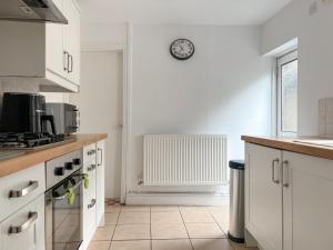 a kitchen with white cabinets and a clock on the wall at Taff's Well Cottage in Taffs Well +14 photos