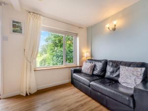 a black leather couch in a living room with a window at The Cottage in Fairlight