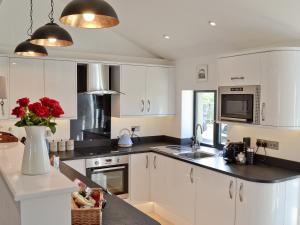 a kitchen with white cabinets and a vase with red roses at Ty Isaf Cottage in Ffair-fâch