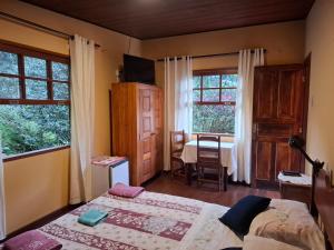 a bedroom with two beds and a table and windows at Pousada Pedra da Gávea in Visconde De Maua