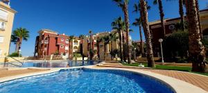 a swimming pool with palm trees and buildings at Casa Rivero in Los Alcázares
