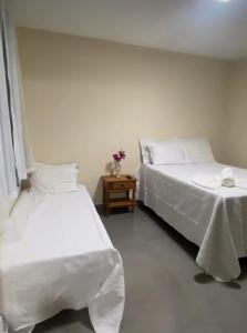 a bedroom with two beds with white sheets and a table at Chácara Vale do Sol in Valença +3 photos