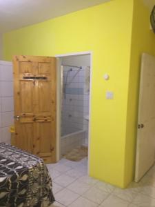 a bedroom with a yellow wall and a bathroom with a shower at Cozy Oasis Hideaway in Port Antonio +16 photos