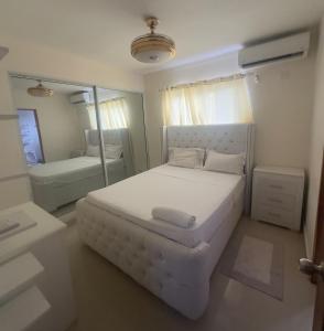 Un dormitorio blanco con una cama grande y un espejo. en El hogar ideal para tu estancia, en Santo Domingo
