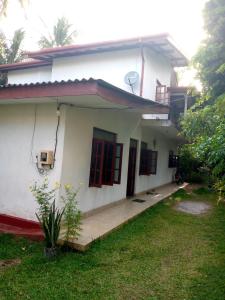 a white house with red doors and a yard at Birdsong Guest House in Ambalangoda